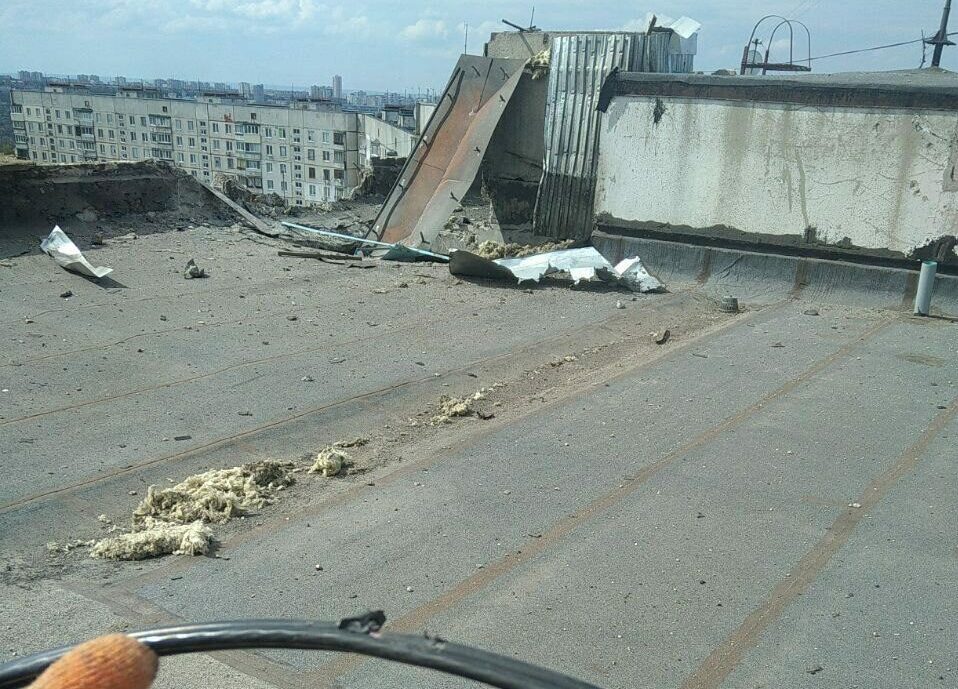 View from a rooftop of a gloved hand holding frayed fiber and showing some destruction on the roof